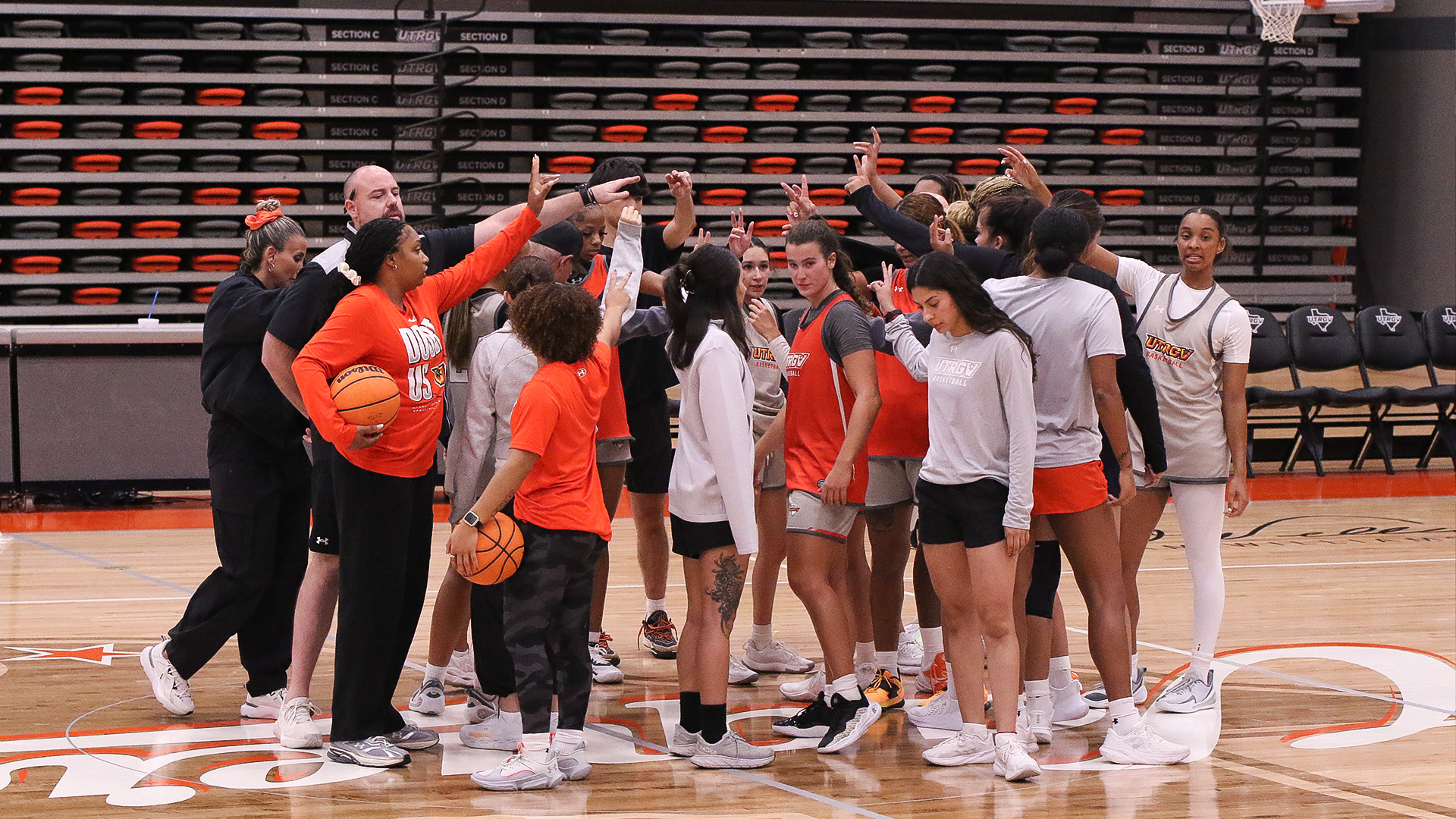 Image is a photo of a women's basketball team huddle from first practice