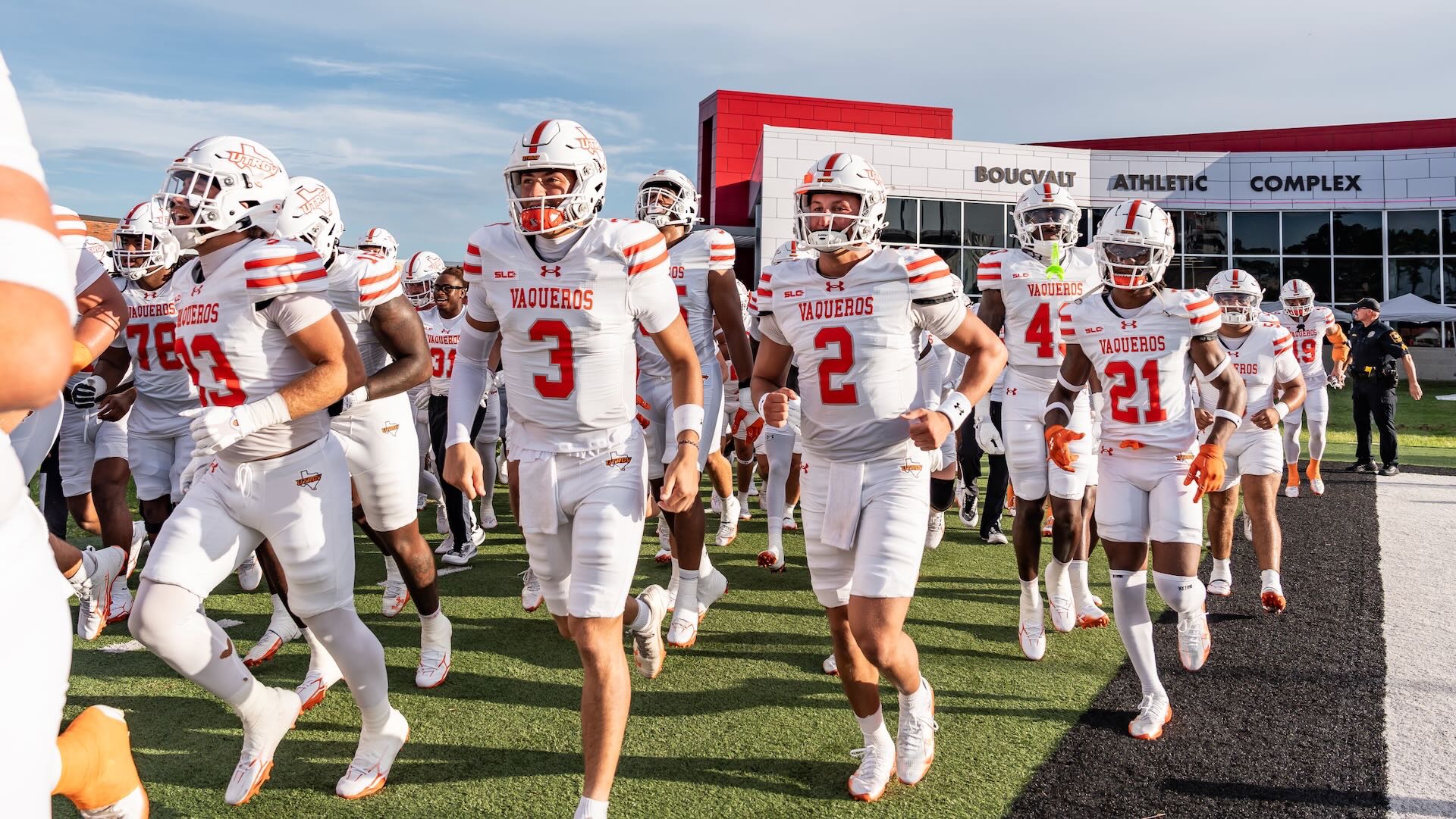 Image shows football players in white jerseys and white helmets running onto a field.