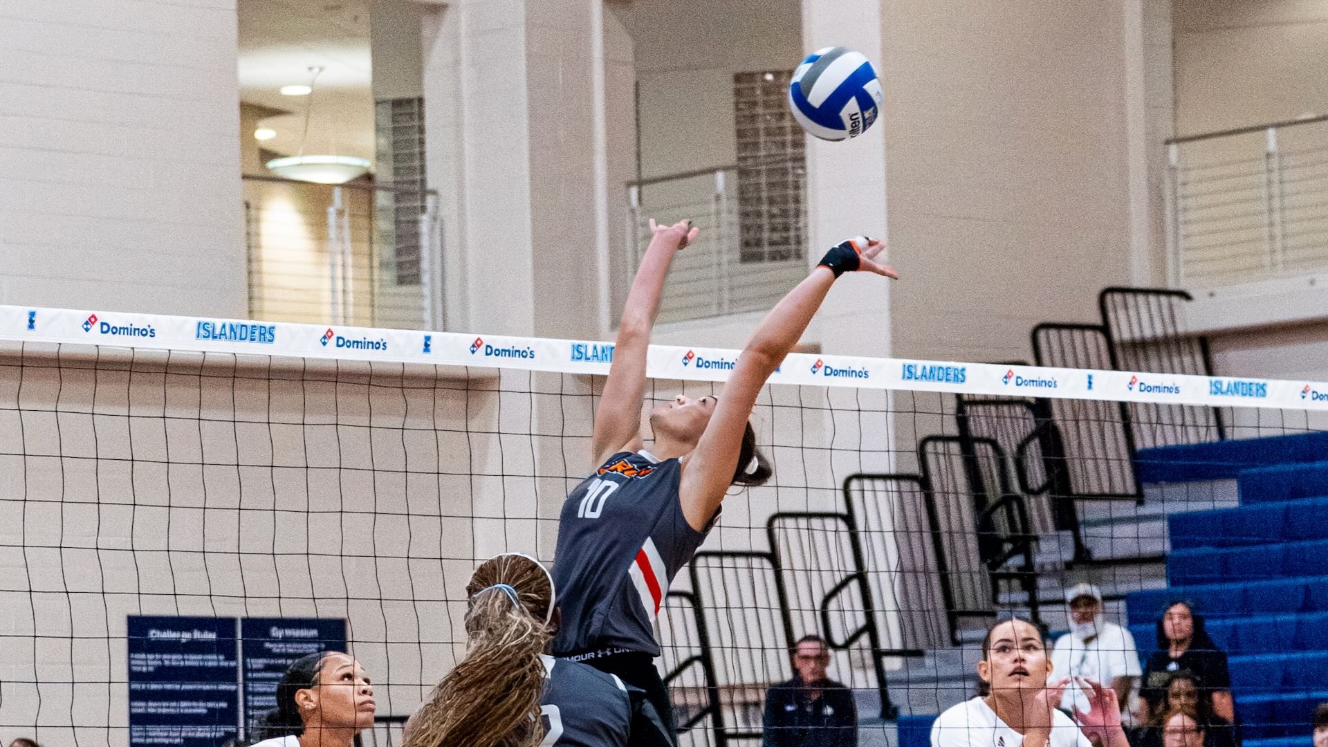 Image shows a volleyball player in a gray uniform wearing #10 setting a ball backward.