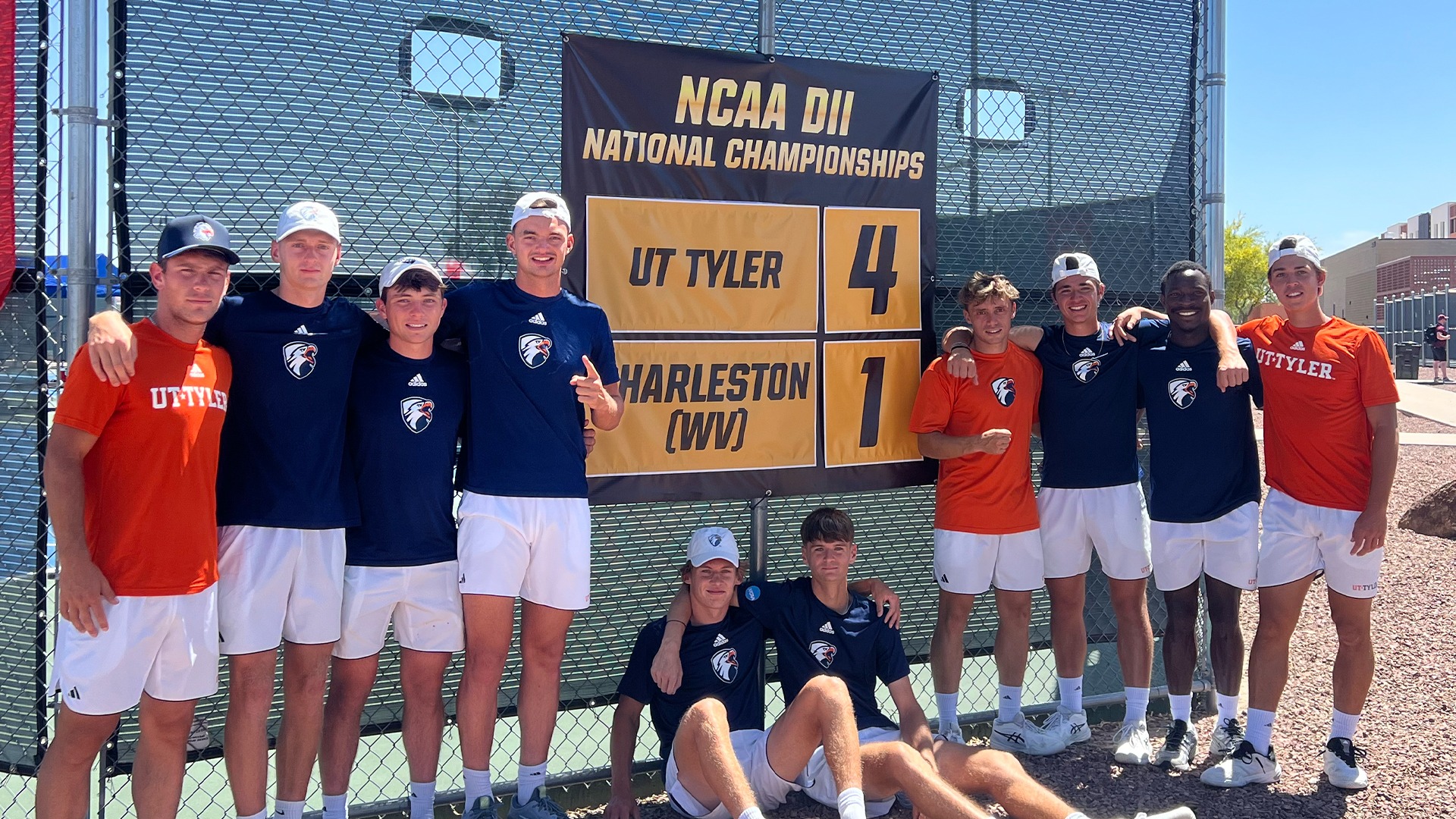 UT Tyler men's tennis poses in front of a scoreboard after beating Charleston in the NCAA Round of 16