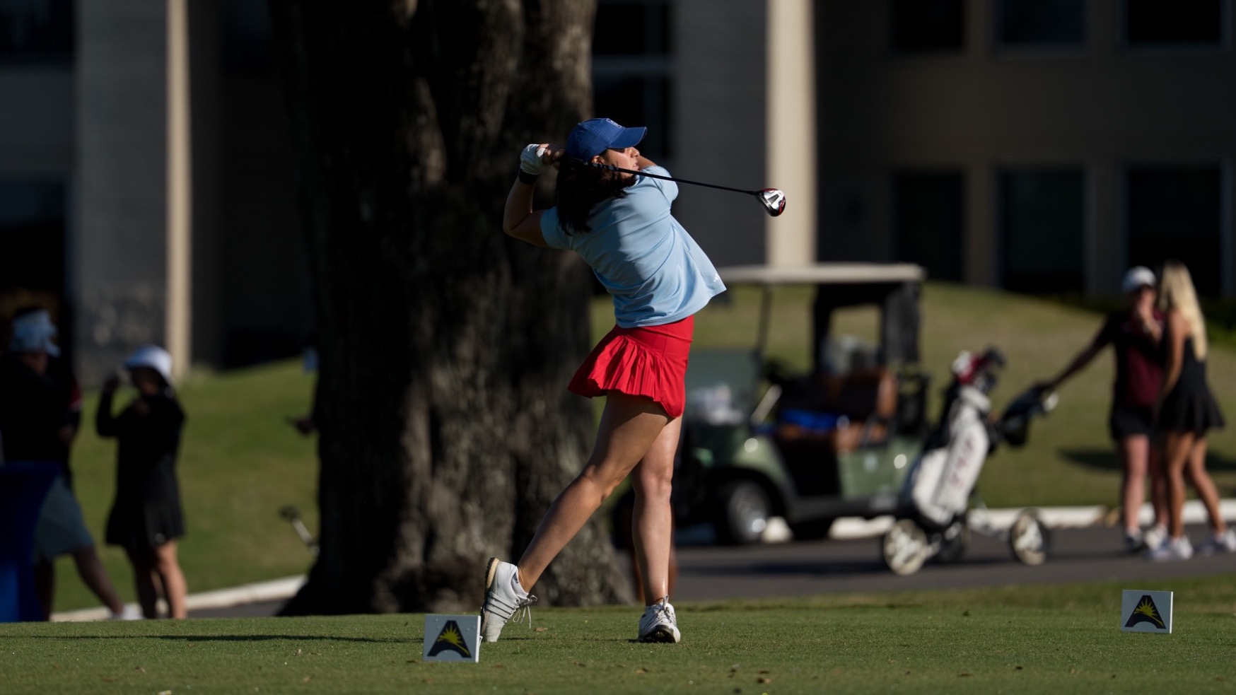 UWG women's golfer Emma Baier tees off on the opening hole of the 2026 ASUN Championships. The junior is wearing a light blue top with a red skort.