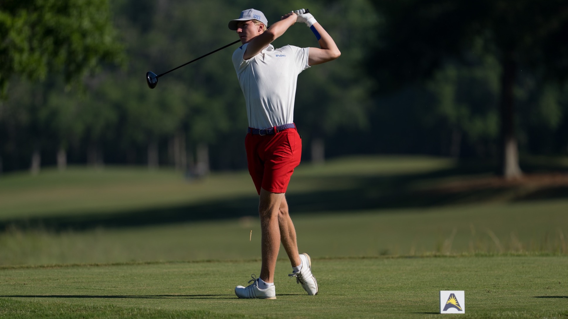 Milton Wallin tees off to begin his 2026 ASUN Men's Golf Championship at Kinderlou Forest Golf Club in Valdosta. He is wearing a white shirt with red shorts.