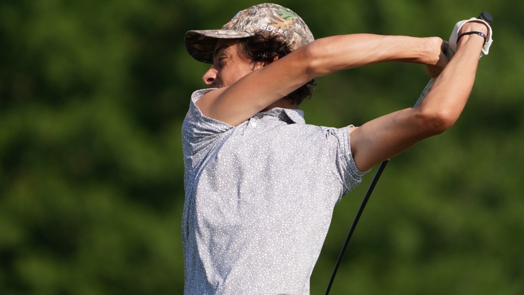 Thomas Romani, wearing a white shirt with a topographical map design and a traditional camo golf hat, tees off in the final round of the ASUN Men's Golf Championship.