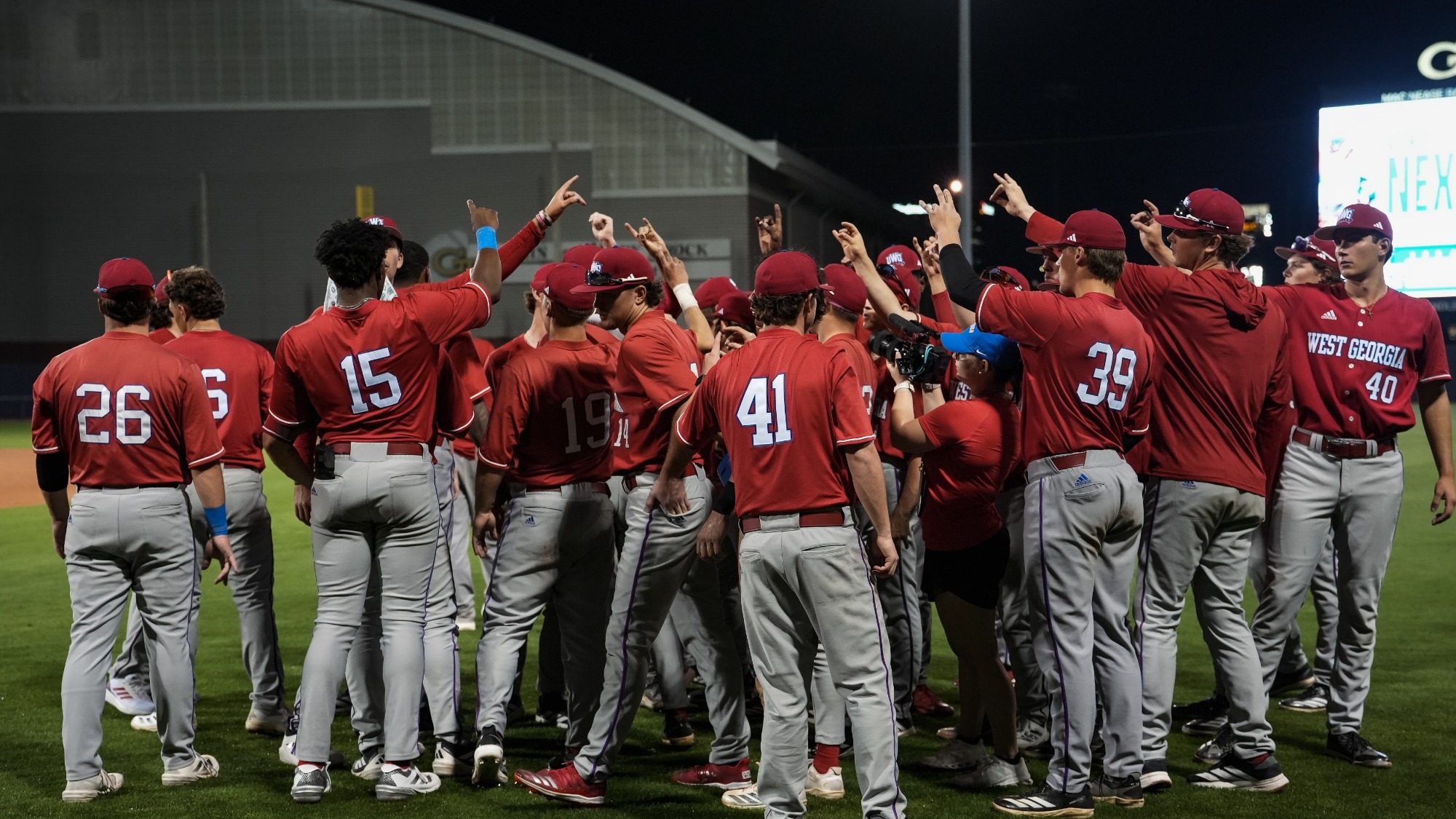 UWG baseball team in red jerseys and gray pants with arms up in the air.