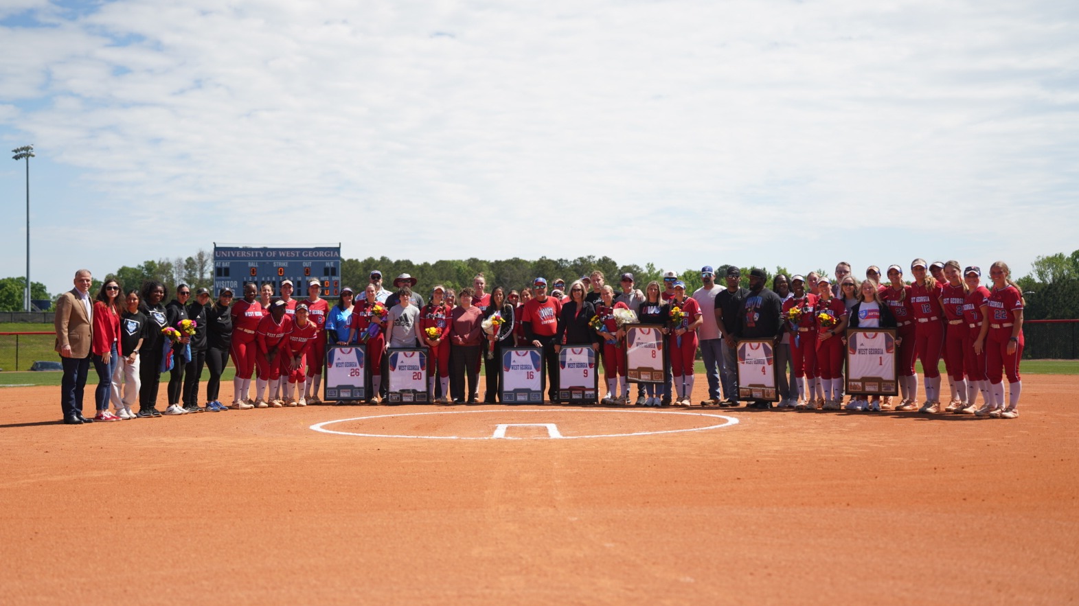 A group of UWG softball stuedent-athlete stands with UWG leadership and their supporters as the team celebrates Senior Day 2026. The seven seniors are holding their framed jerseys.