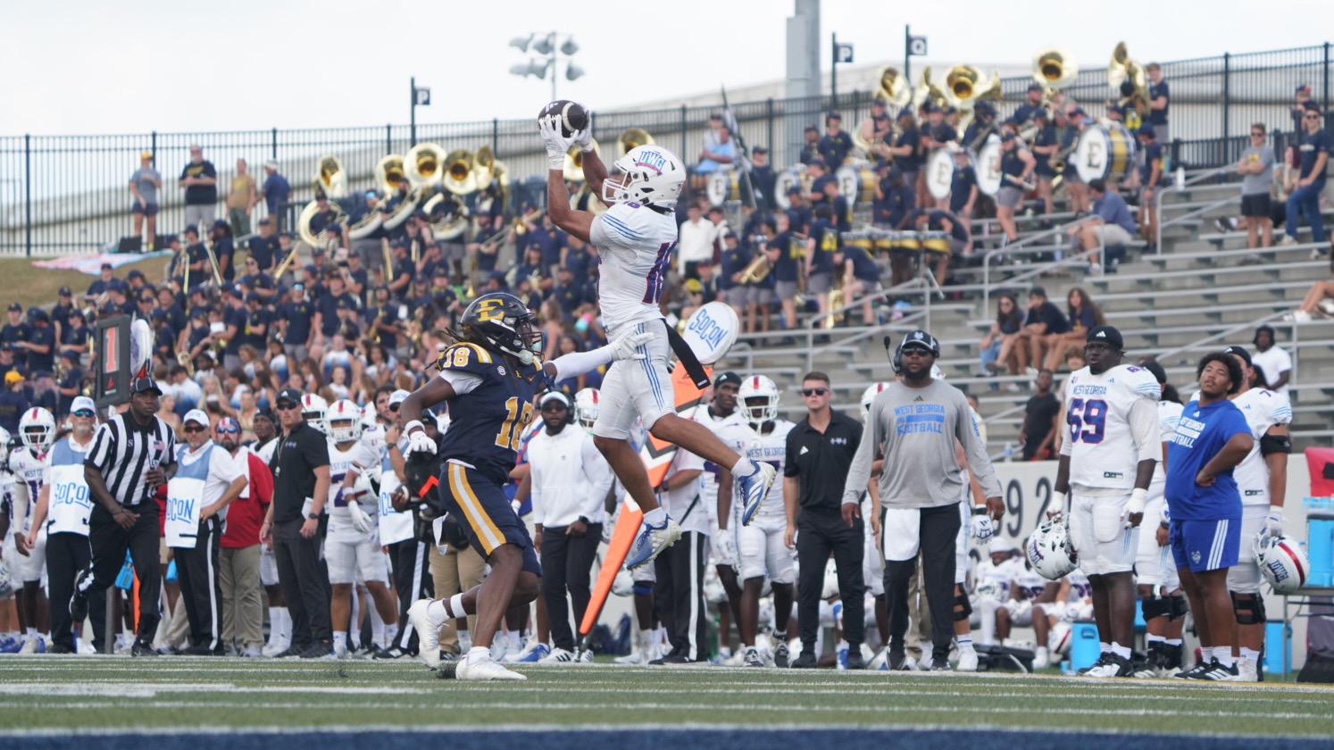 Brody Jones jumps in the air to catch a ball in the Wolves' road game at ETSU. Jones is wearing all white uniform with a white helmet with the UWG logo on the side.