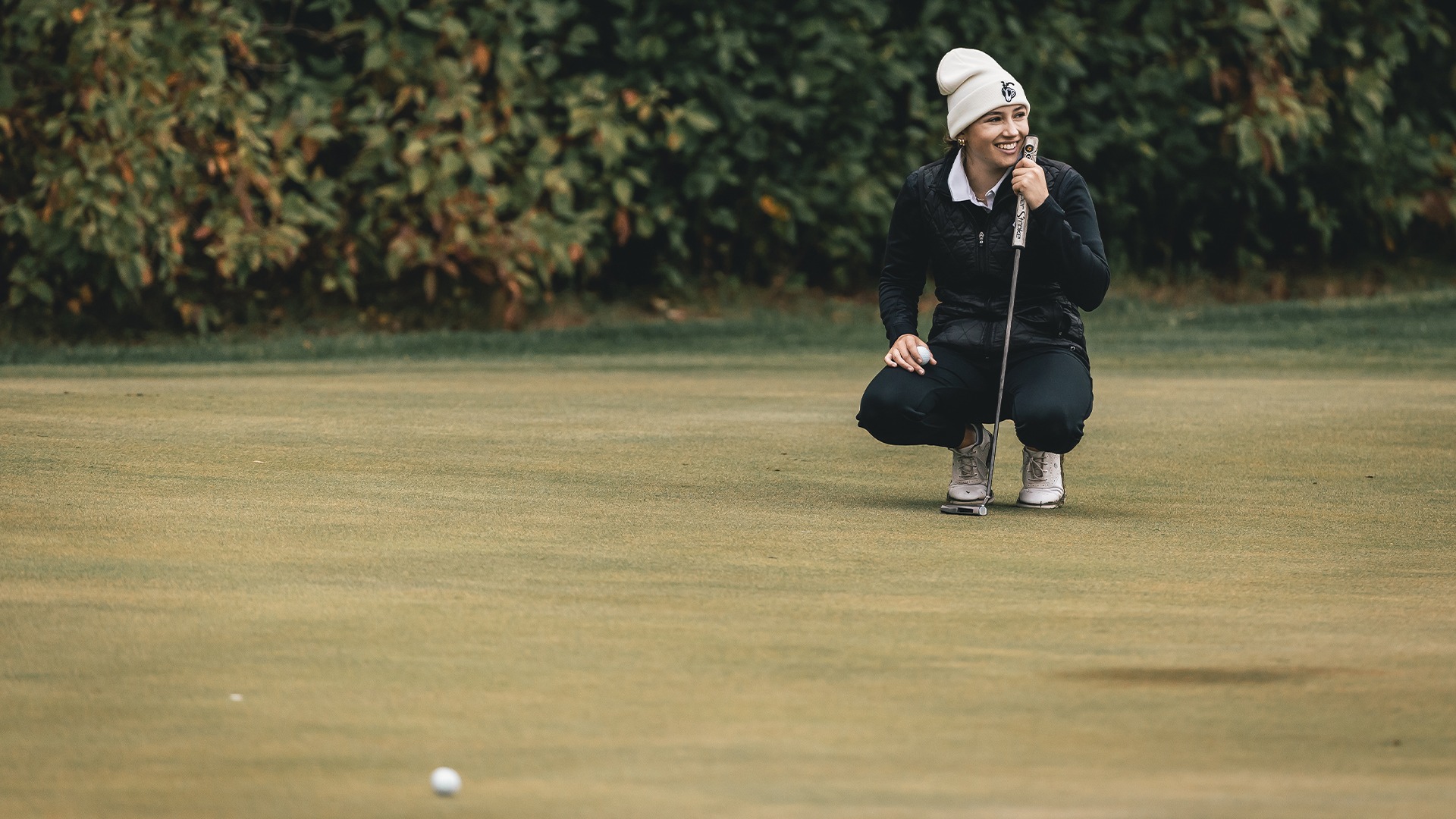 Olivia Weyenberg smiling on the green crouched down.