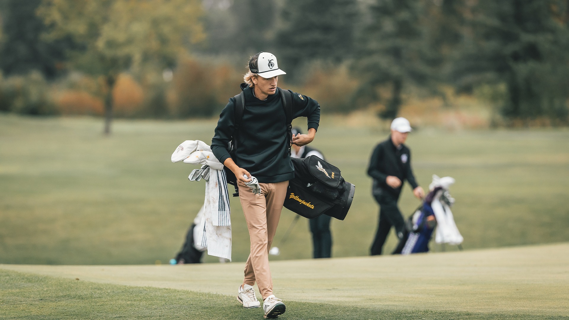 Colton Stupar walking around the green with his golf bag on his back.