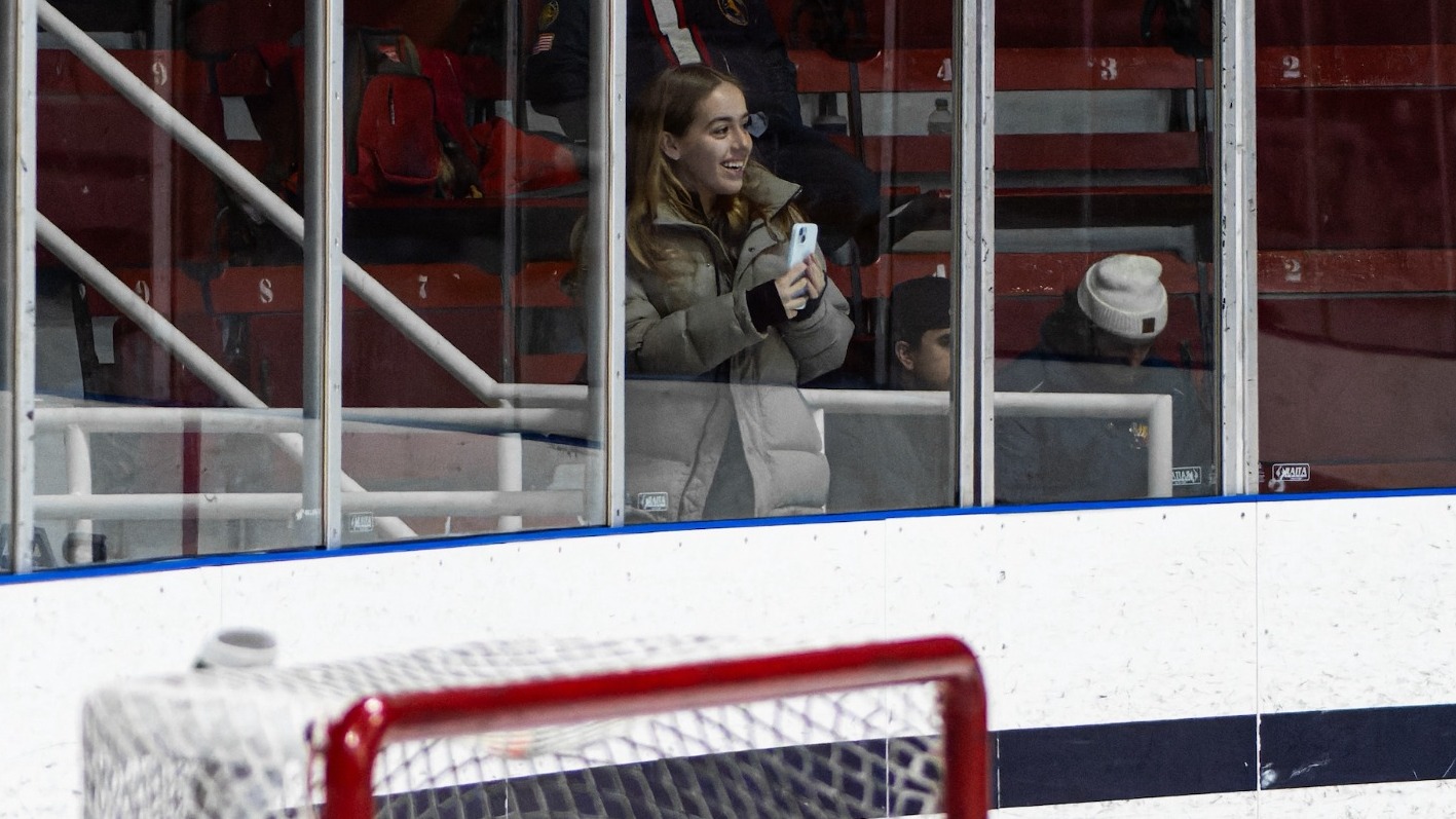 Julieta standing behind the glass capturing Varsity Blues men's hockey content