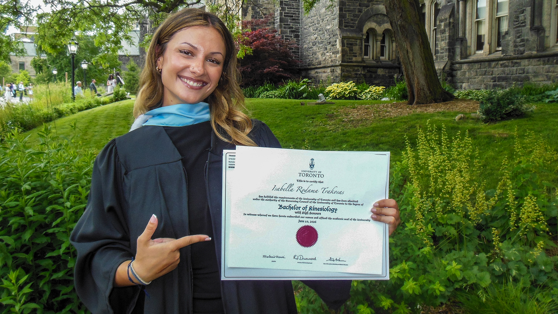 Isabella Trakosas poses with her diploma on campus