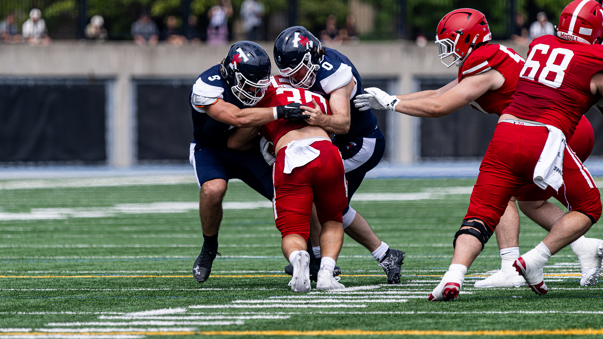 Two Varsity Blues football players tackle a McGill Redbird