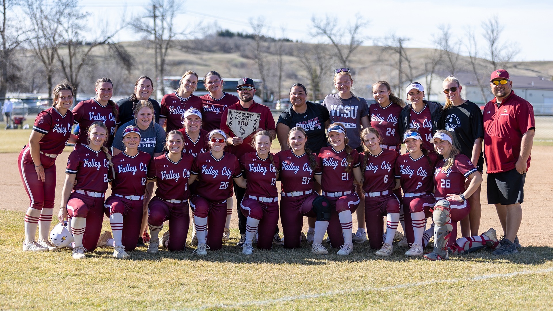 VCSU softball poses with head coach Matt Gable after 100th career win.