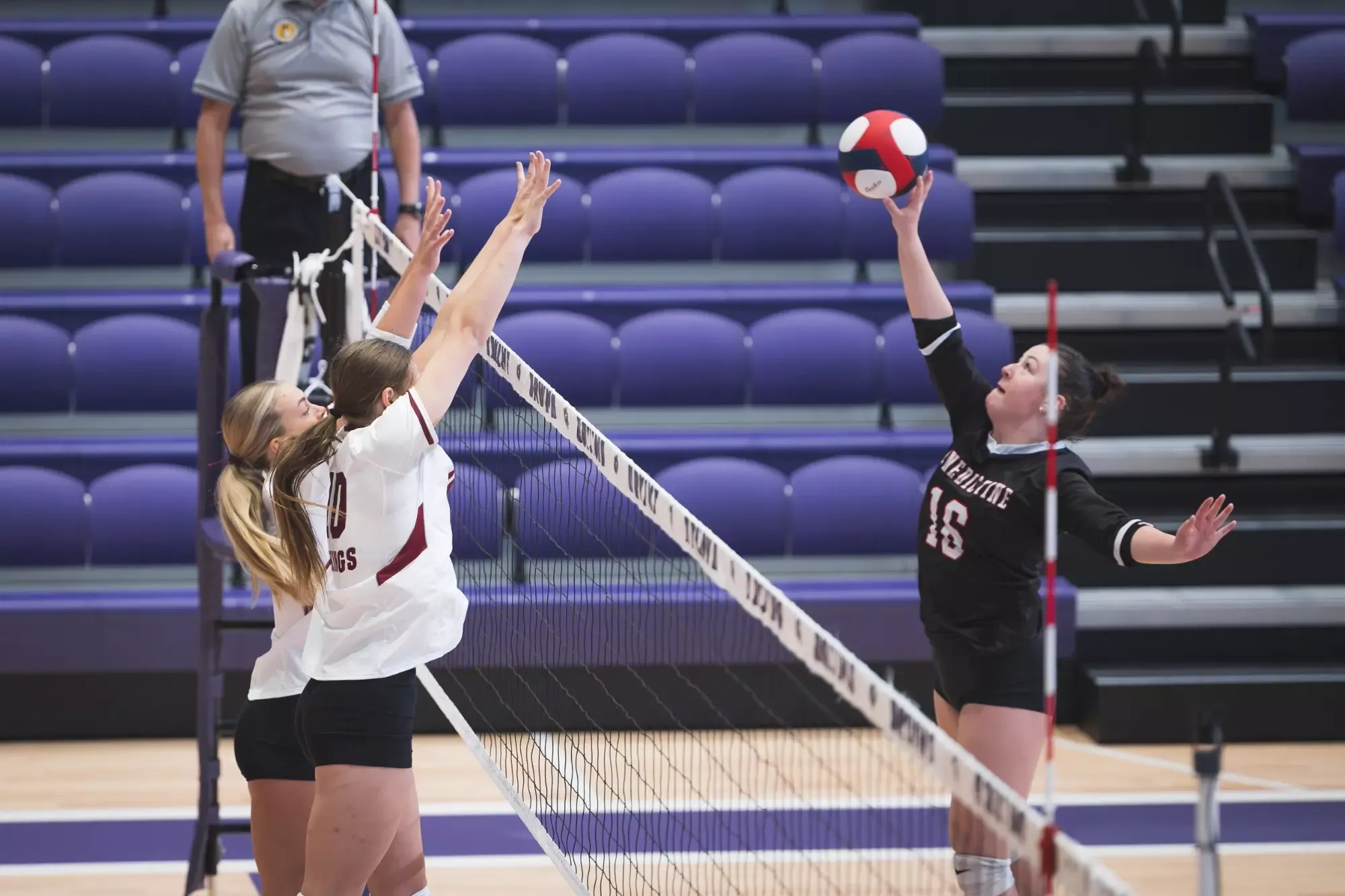 Two VCSU blockers jump as an opposing player attacks the ball at the net.