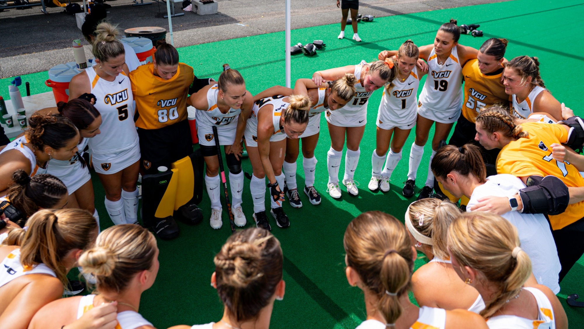 The VCU Field Hockey Team Huddles in a circle wearing white uniforms before a game