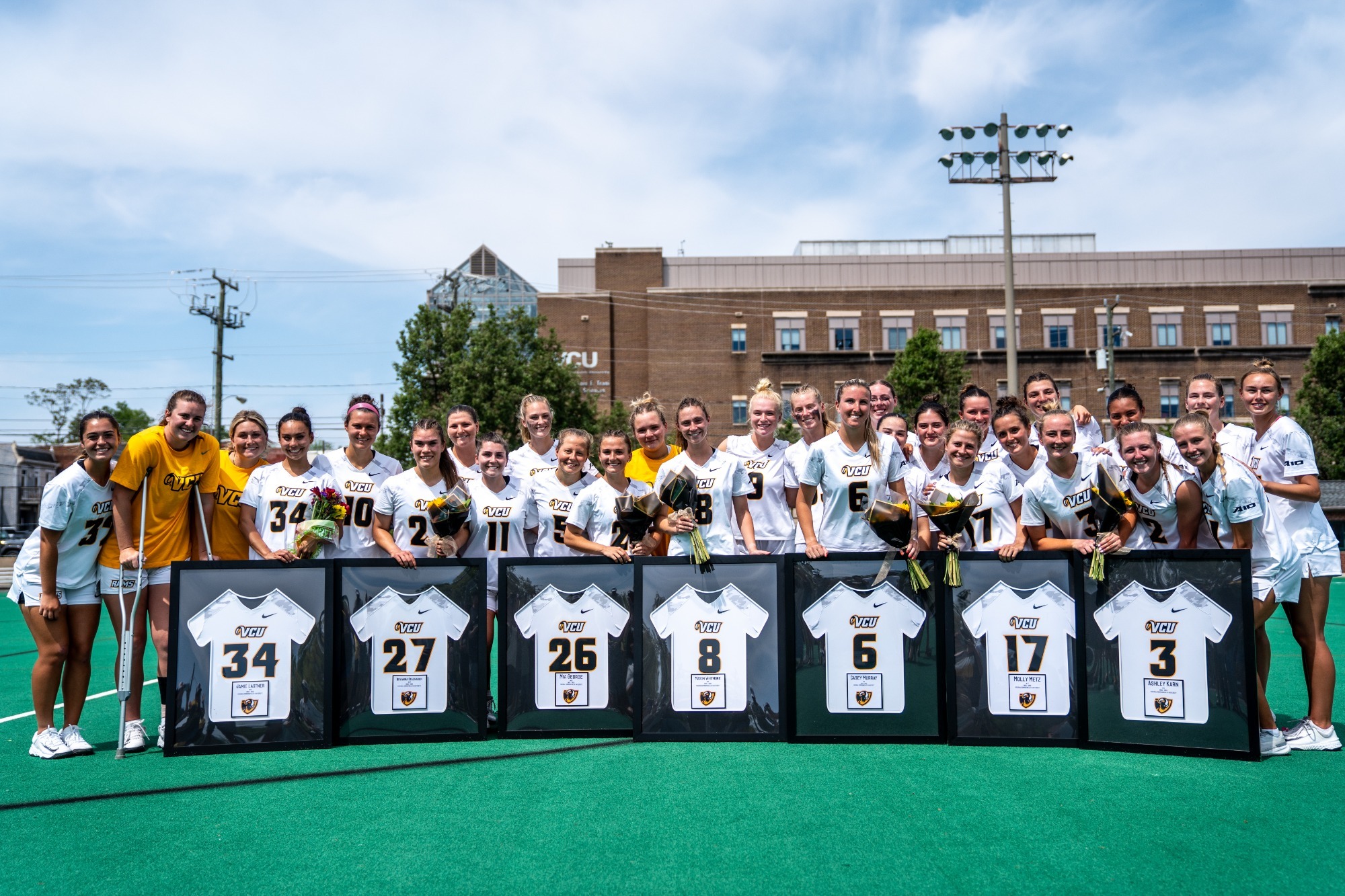 A photo of the seven 2025 VCU Seniors posing with framed uniforms and surrounded by the entire team