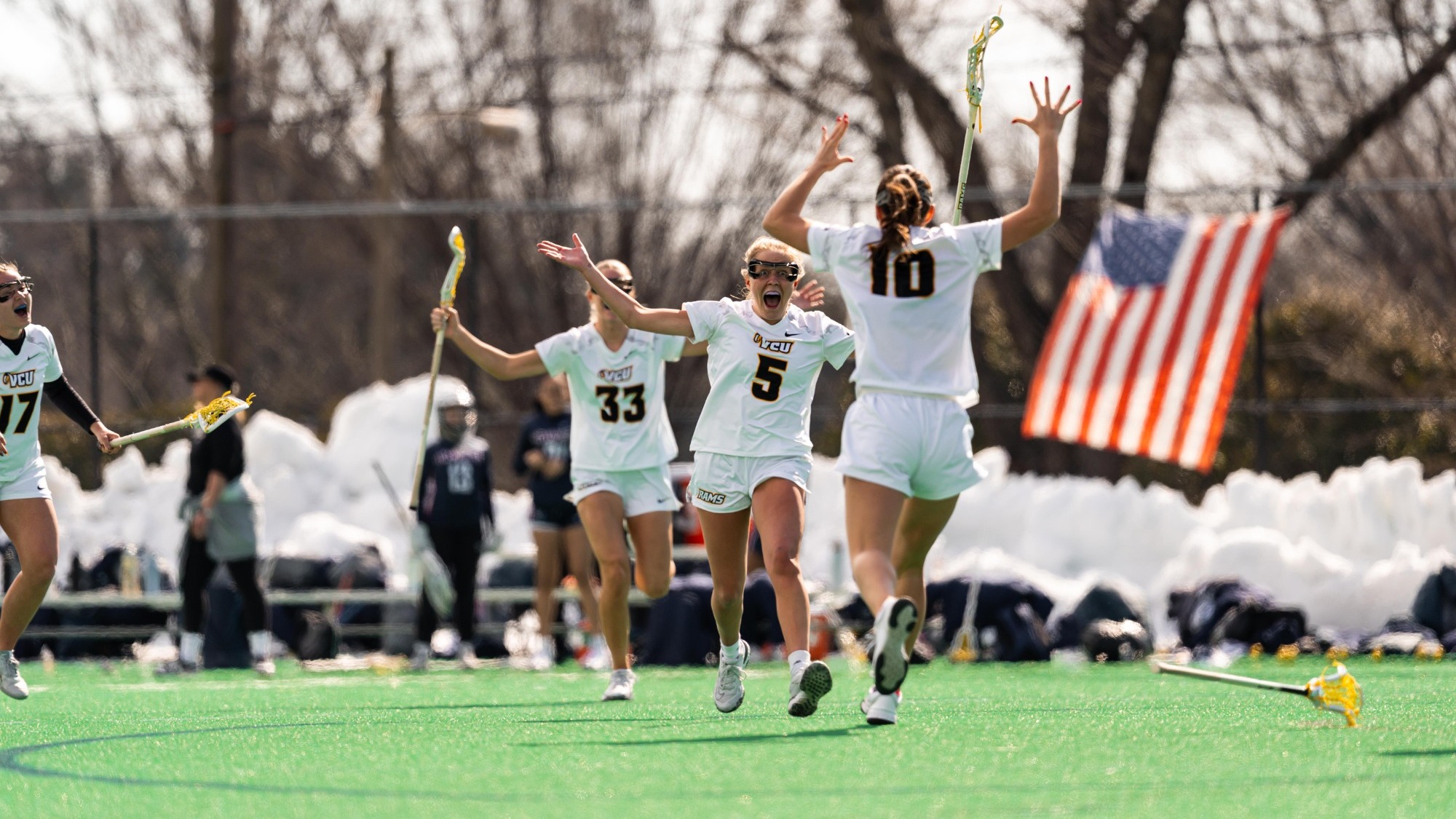 Rachel Koeneke and Ally Schromsky of VCU Lacrosse both wearing white uniforms celebrate after scoring against Howard