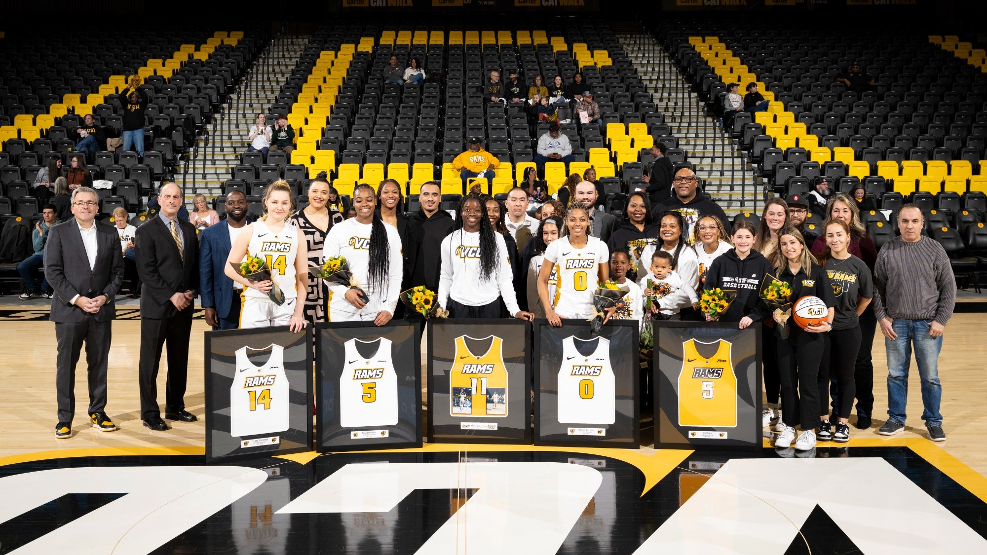 A group of VCU Women's Basketball Seniors and their families stand at halfcourt for a photo following the Senior Day Ceremony