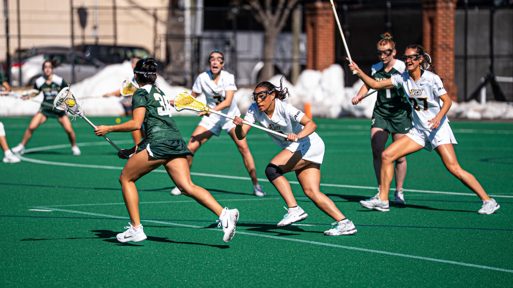 Kennedy Lee of VCU wearing a white #1 jersey guards a Charlotte lacrosse player in a game