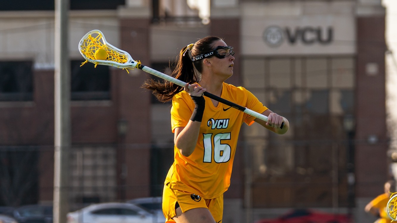 Kate Unzicker of VCU wearing a gold #16 jersey cradles the lacrosse ball in a game against Longwood