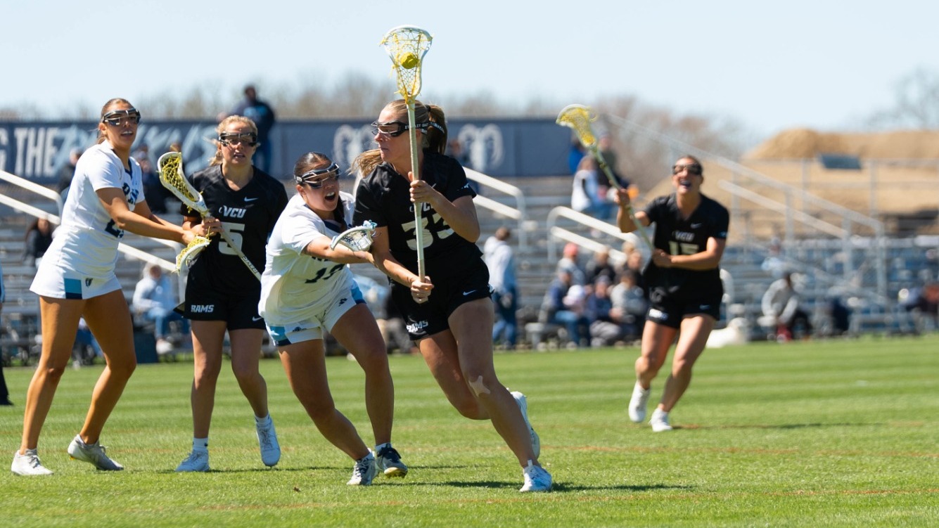 Sam Palmer of VCU wearing a black #33 jersey cradles the ball running while being guarded by a Rhode Island defender
