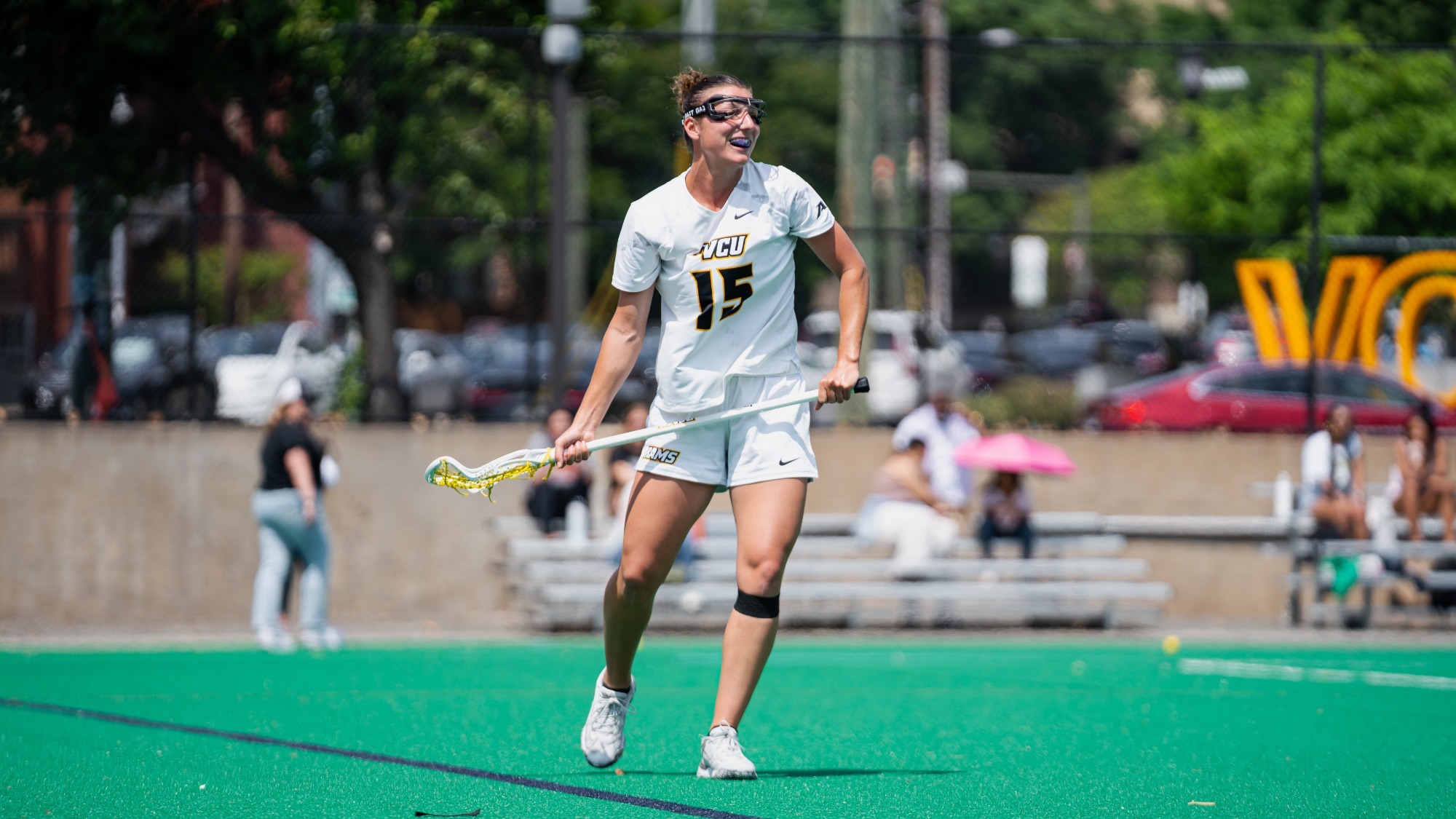 Ameila Eilbacher of VCU wearing a white #15 jersey smiles holding her lacrosse stick during a win over George Mason