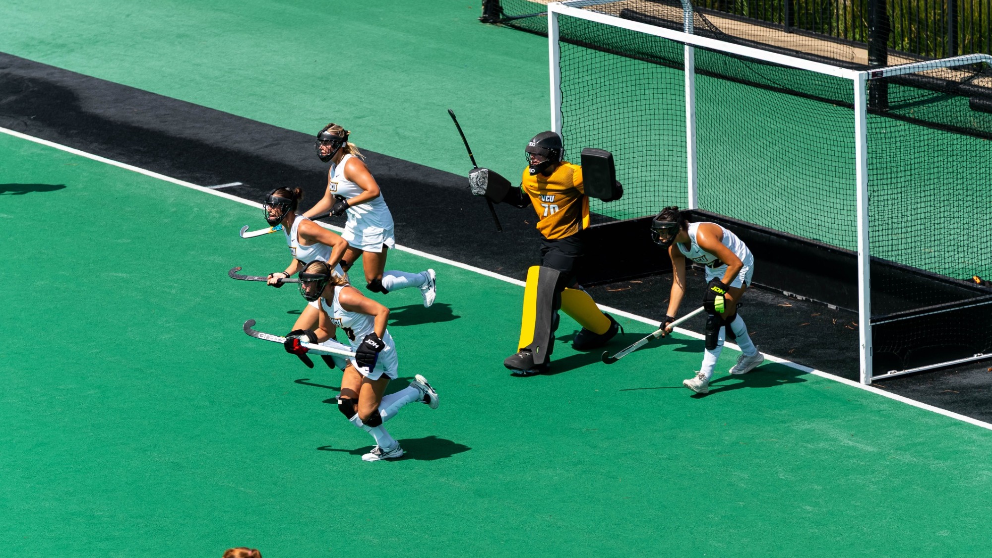 VCU Field Hockey defends a penalty corner wearing gold uniforms charging out from goal