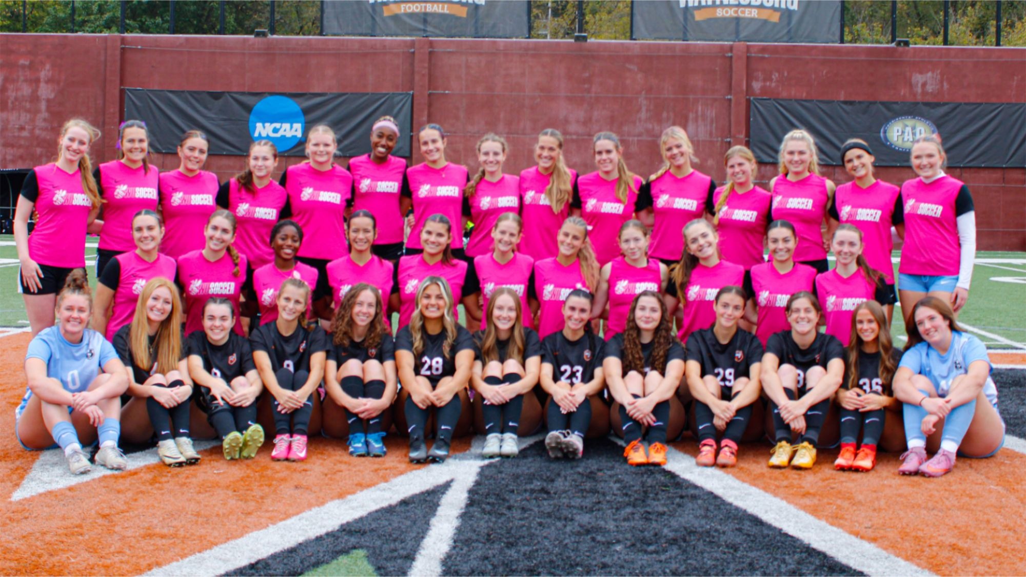 Waynesburg team picture with the seniors on the team sitting in the front row and the rest of the team behind them in pink