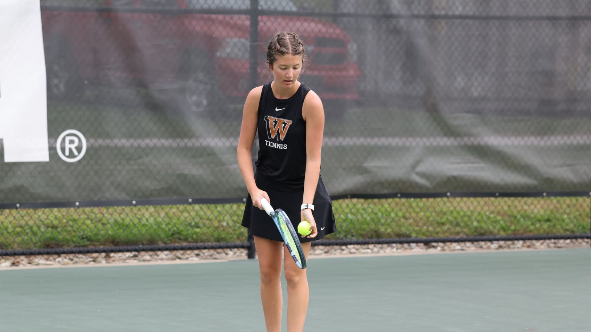 Taylor Stephens looks down at her raquet and tennis ball as she prepares to serve