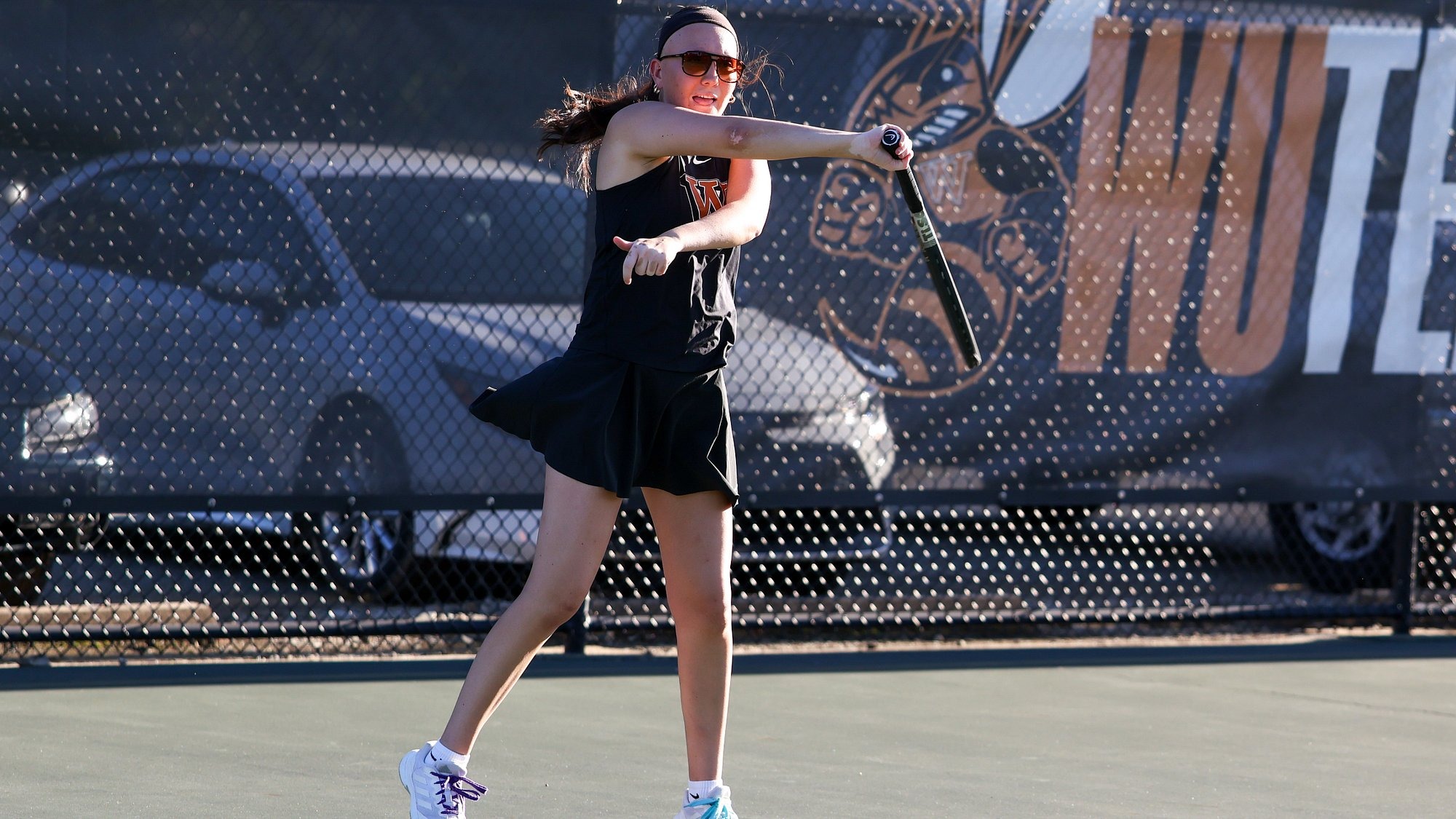 Julia Luzar, wearing sunglasses, follows through on a forehand swing