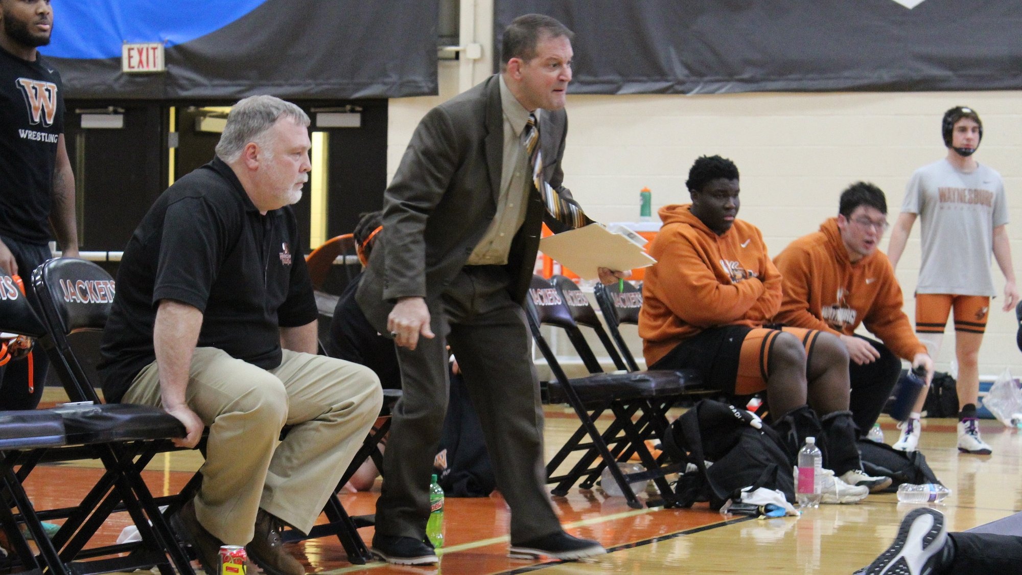 Head coach Bobby Patnesky coaching from the bench surrounded by wrestlers and other coaches
