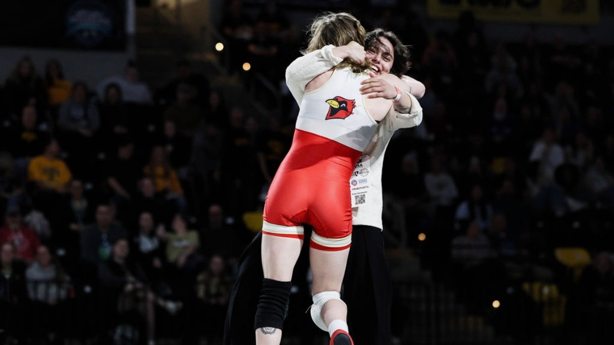Leila Castro hugging and lifting an Otterbein wrestler while smiling on the sideline