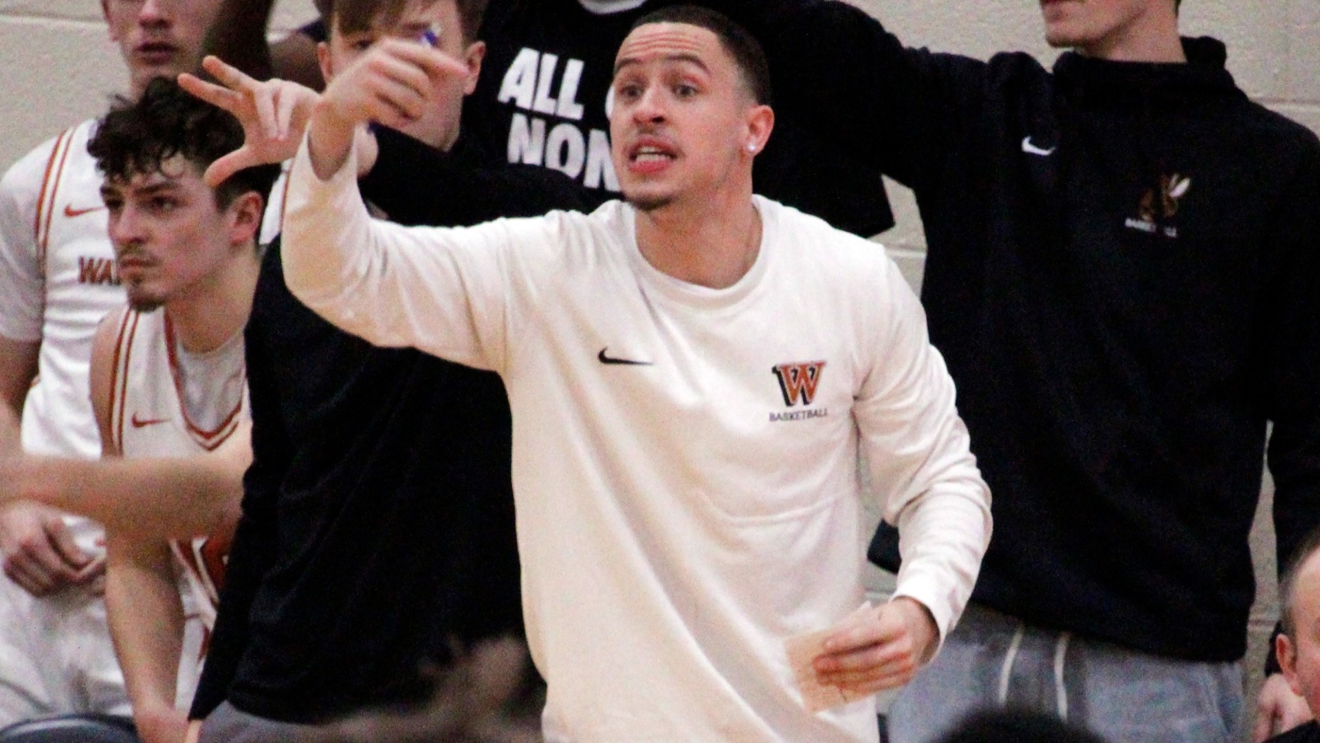 Korey Mitchum gesturing to the players on the court with other players behind him in black shirts and white jerseys