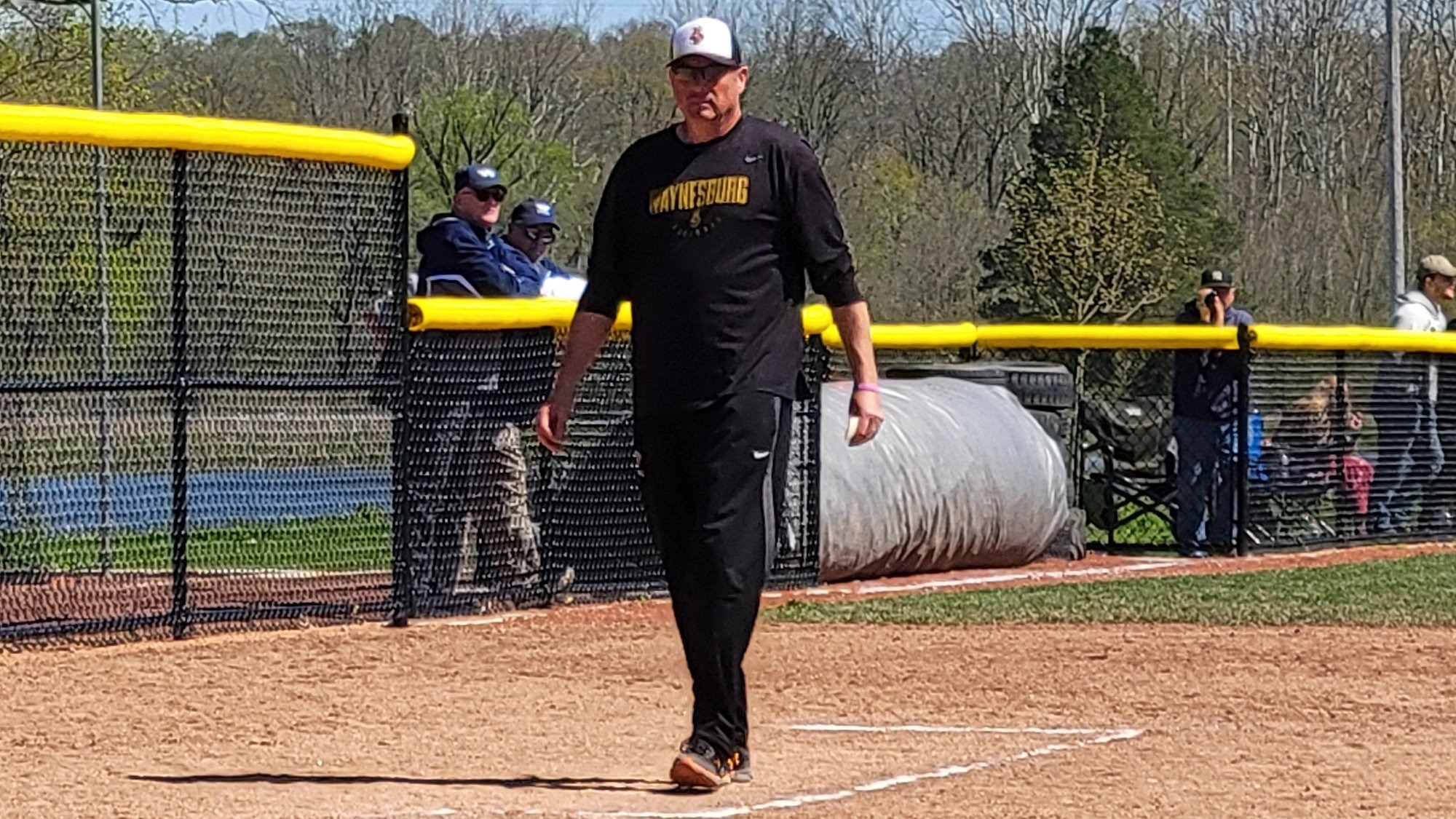 Brett Shimek in black coaching gear walking towards the plate from the third base coaching box