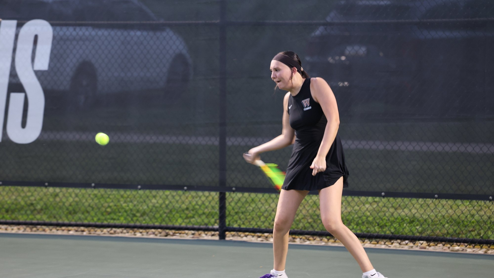 Waynesburg women's tennis player Julia Luzar, wearing a black tennis dress, hits a forehand shot