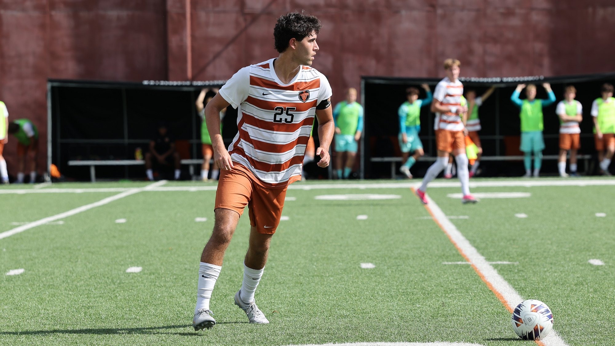 Waynesburg men's soccer player Gabe Bowman in an orange and white striped uniform looks upfield