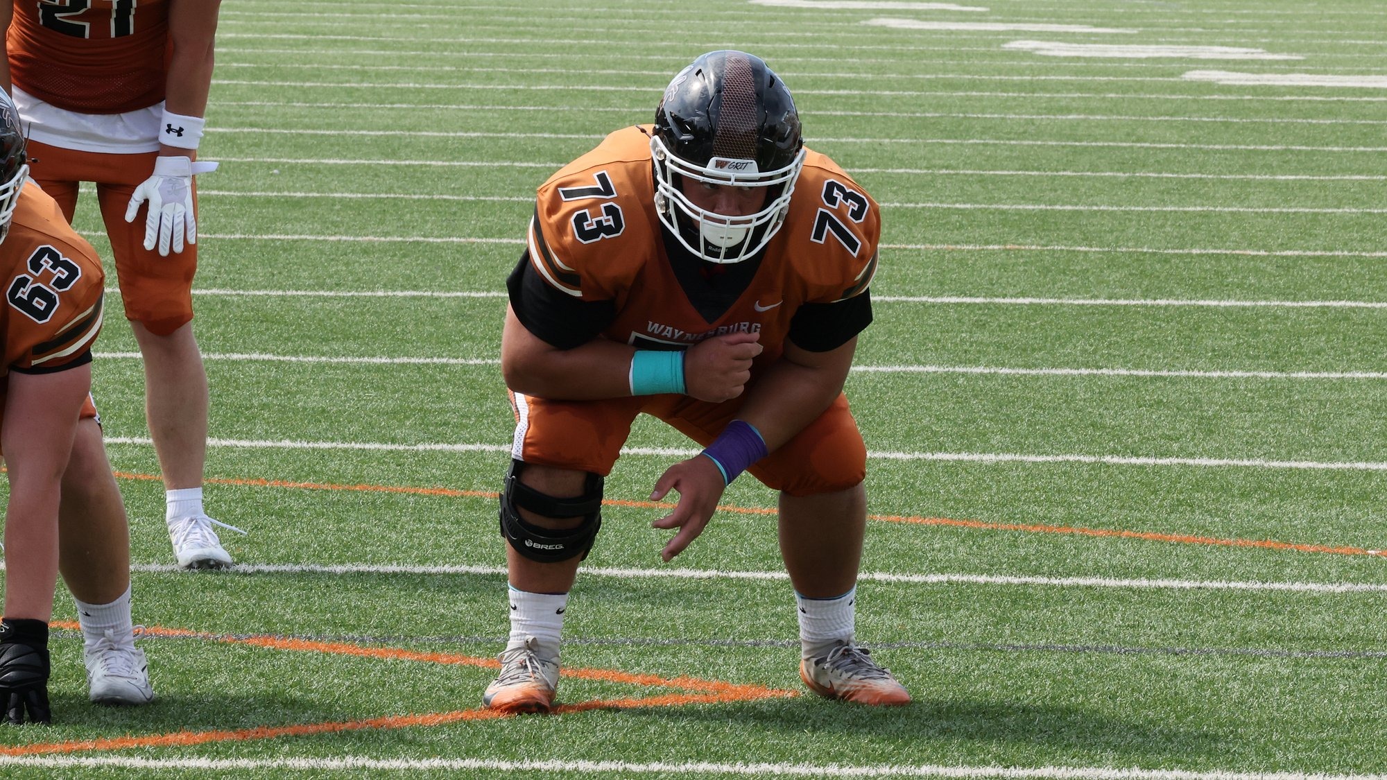 Waynesburg offensive lineman Lucas DeLoatch, wearing an all orange uniform, gets into his pre-snap stance
