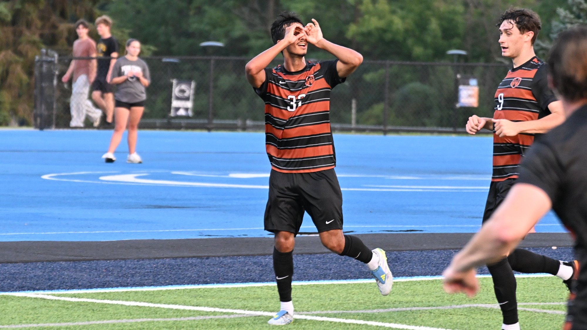 Waynesburg men's soccer player Antonio Baires celebrates scoring a goal with Penn State Altoona's light blue field in the background.