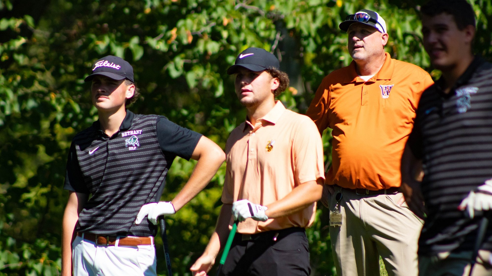 Four men's golfers and Waynesburg head coach Mike Cipoletti stand and look off into the distance