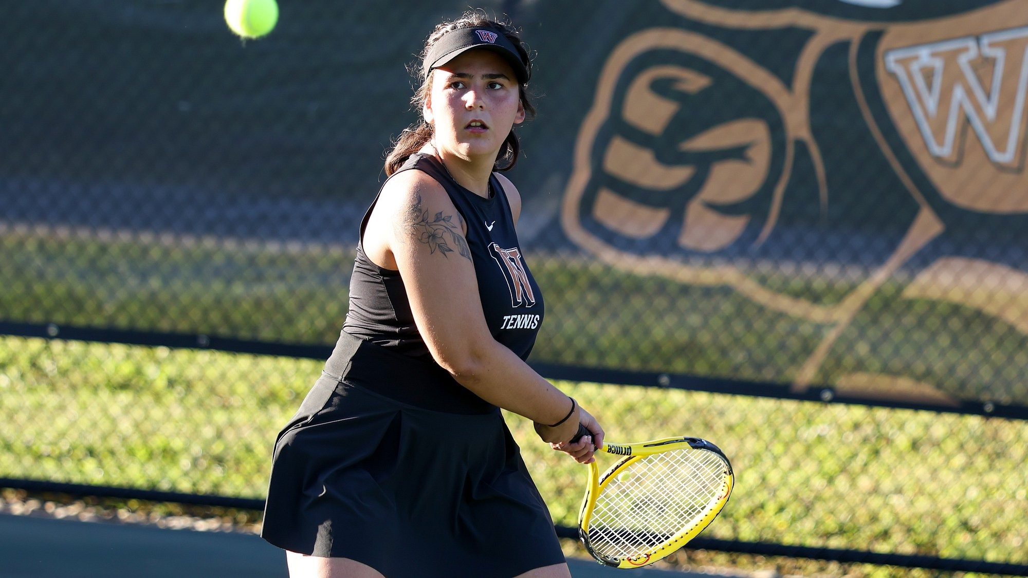Women's tennis player Karly Starcher eyes up the tennis ball in anticipation of delivering a backhand shot