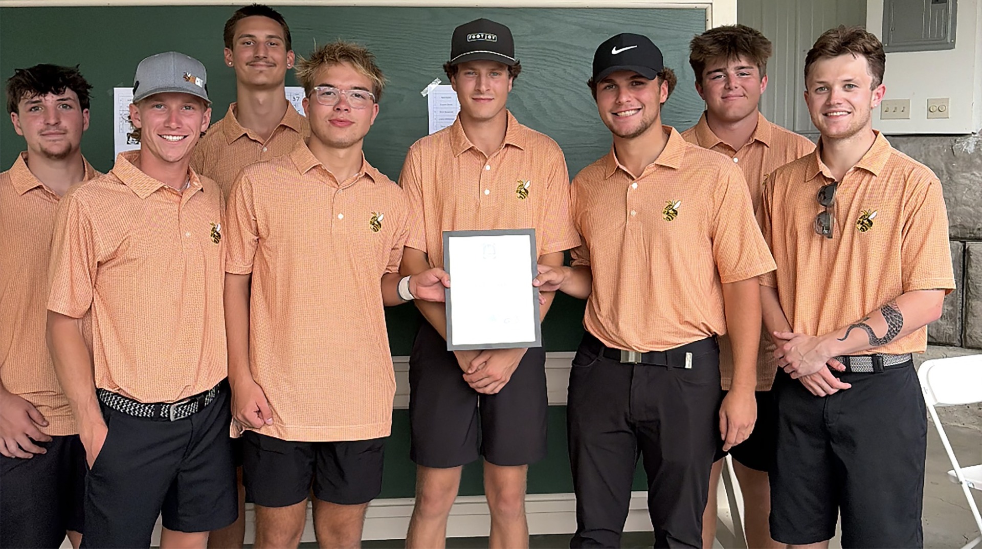 The Waynesburg University golf team dressed in orange golf shirts pose with their plaque for winning their home invitational