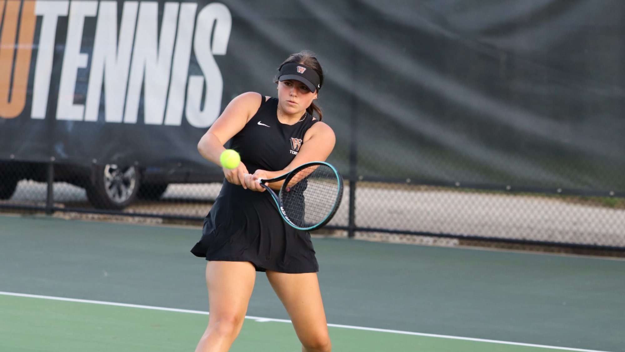 A Waynesburg women's tennis player in a black tennis dress hits a backhand