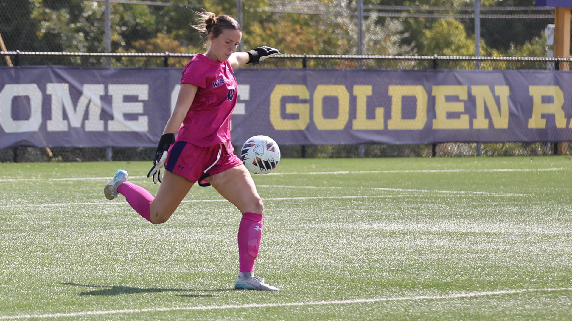 Grace Keen women's soccer goal keeper passing ball out mid game in all pink uniform 