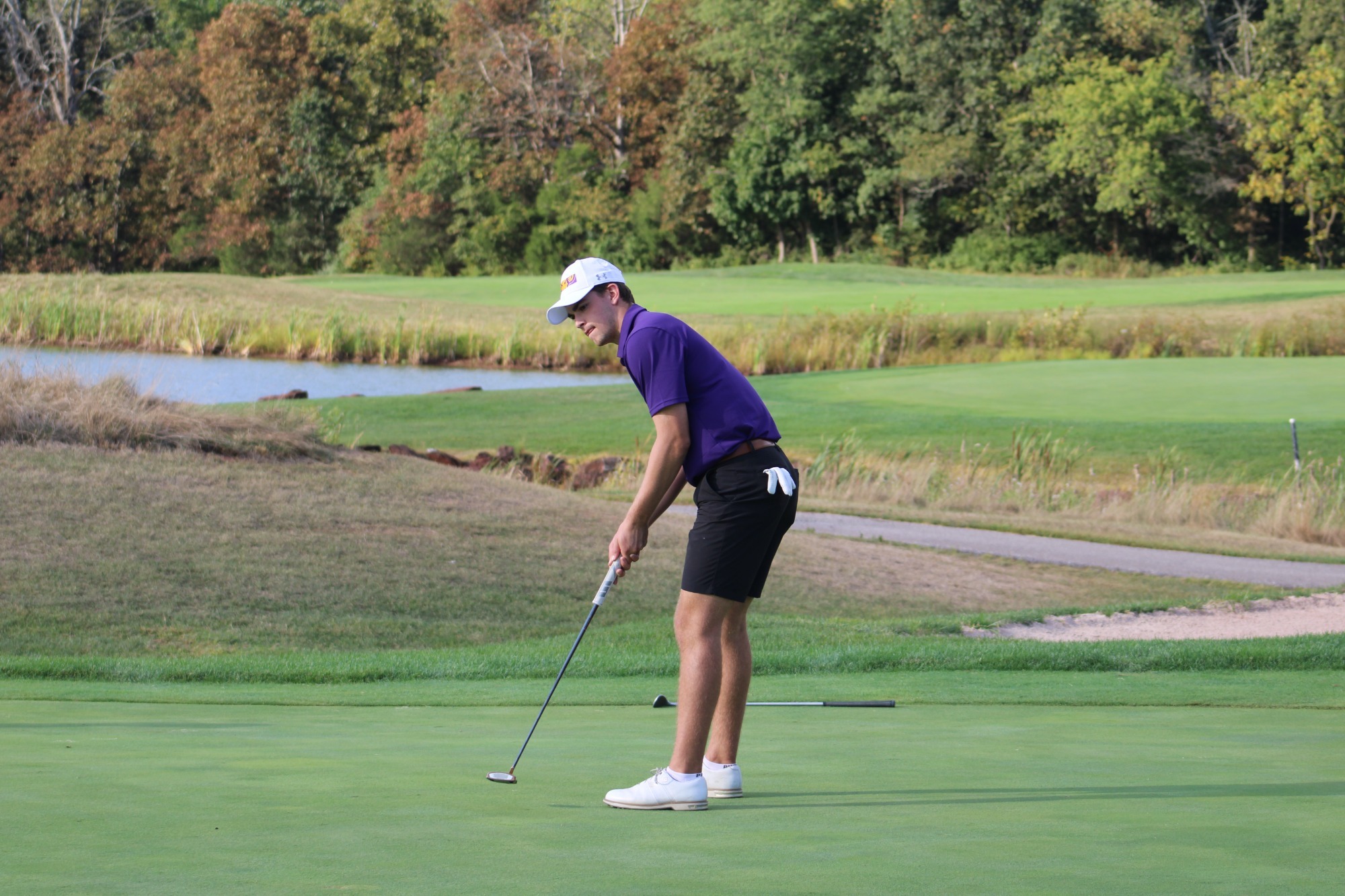 Hilton PUTTING ON GREEN WEARING TEAM ISSUED WHITE HAT, PURPLE SHIRT, AND BLACK SHORTS