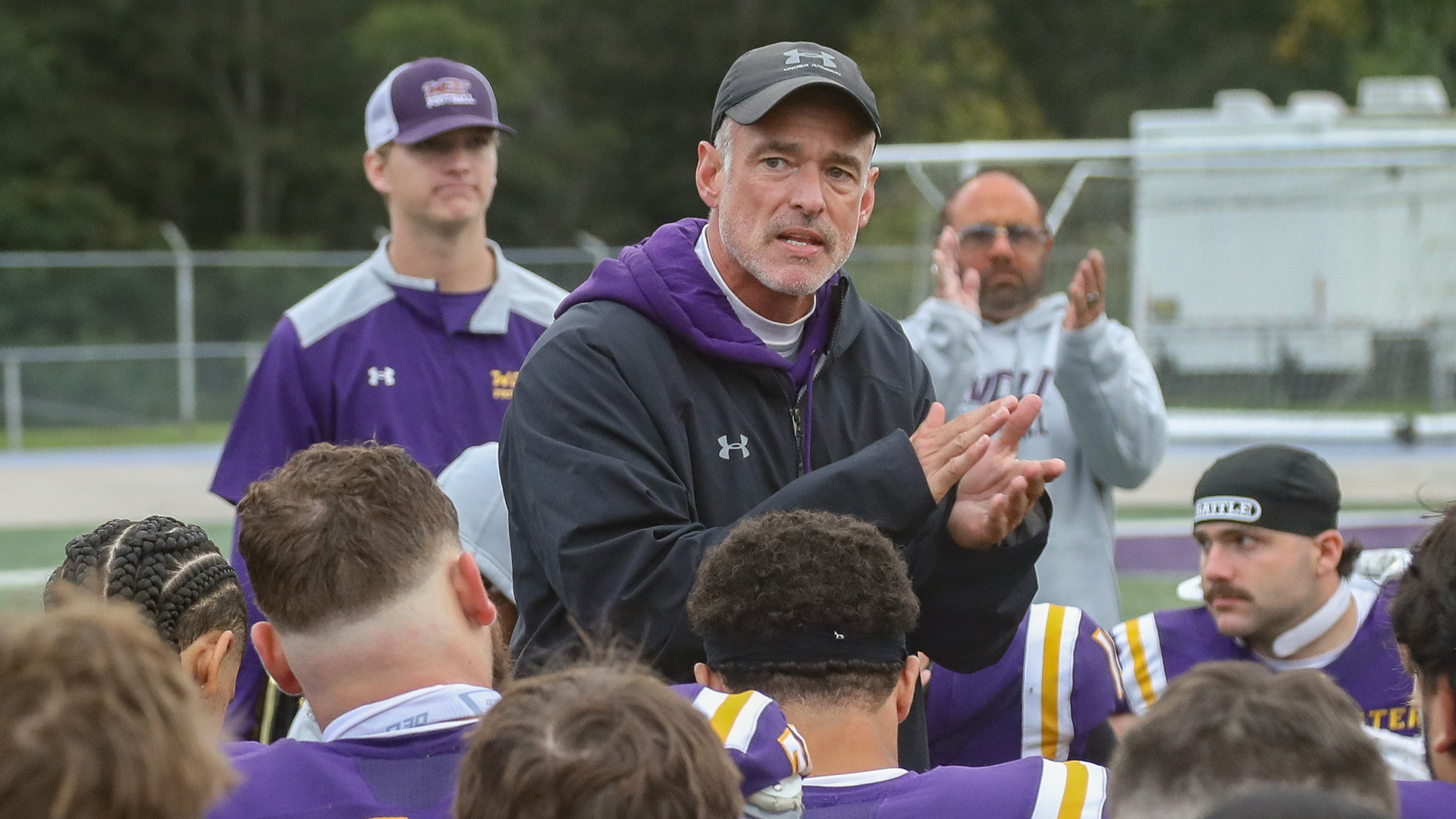 Duke Greco talks to his team after the Millersville game on Homecoming in his black rain jacket with a WCU hat on