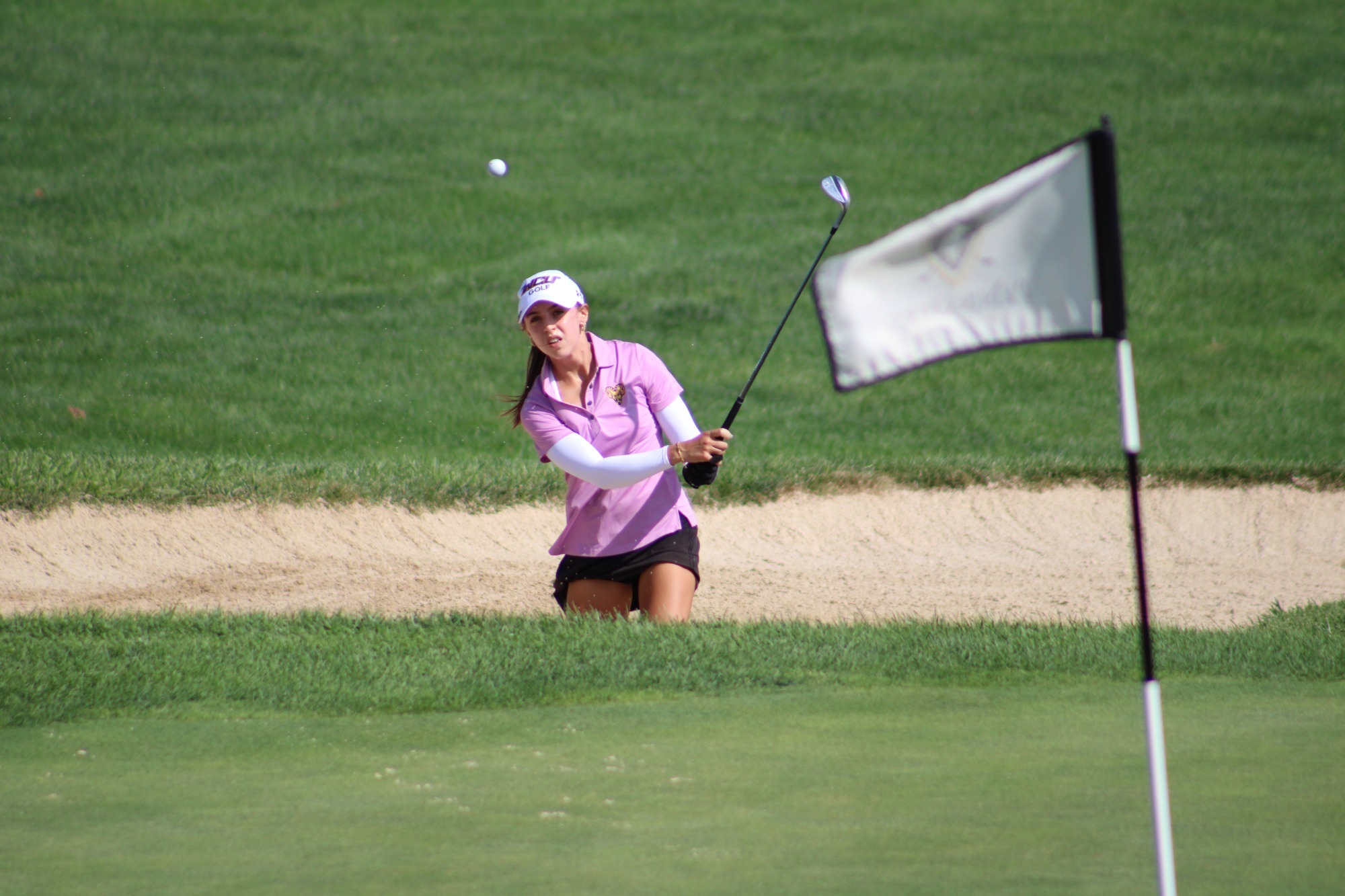 emerson glending wearing pink WCU golf polo with black hat and black skirt chipping out of greenside bunker at penn oaks
