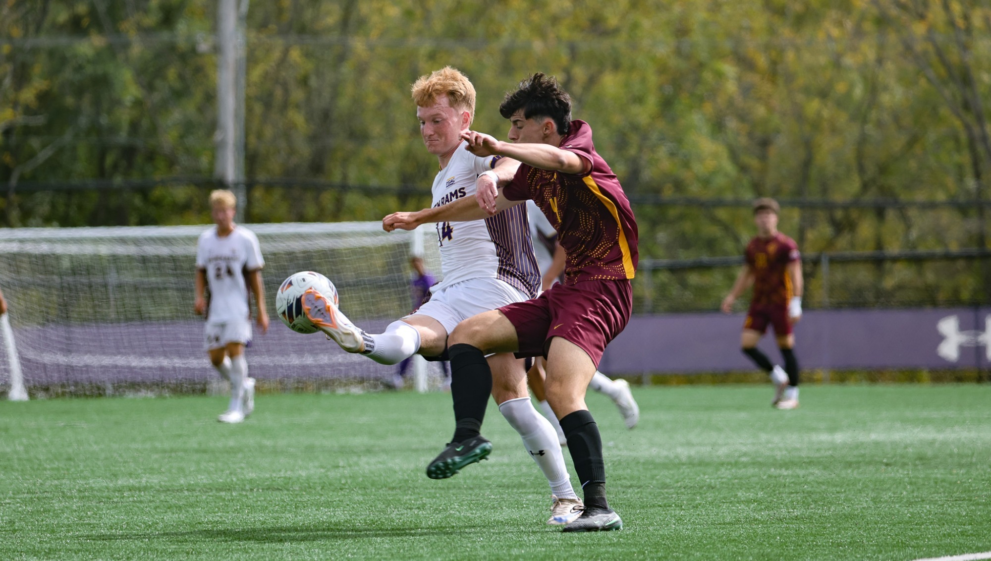 Peter Tichy wearing home white on white plays a 50-50 ball past a Gannon defender wearing maroon road kits