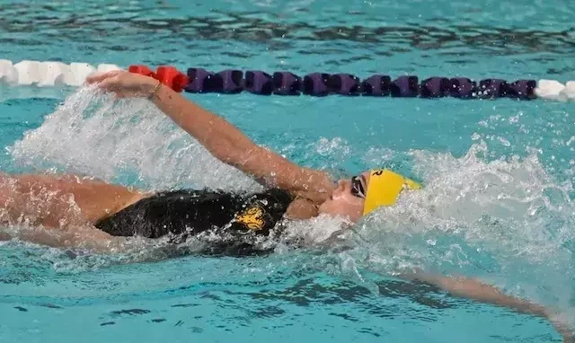 Allie DeFrehn swims the backstroke in her black suit and yellow TYR swim cap and goggles