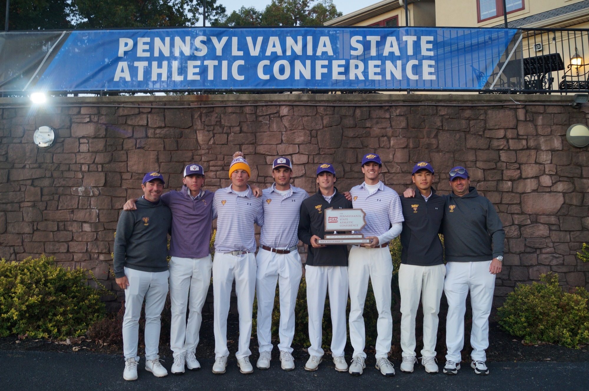 MEN'S GOLF TEAM WITH COACHES CHRIS MERCE AND SEAN GLYNN POSING WITH PSAC SECOND-PLACE TROPHY IN FRONT OF PSAC CHAMPIONSHIPS BANNER AT IRON VALLEY IN LEBANON PA