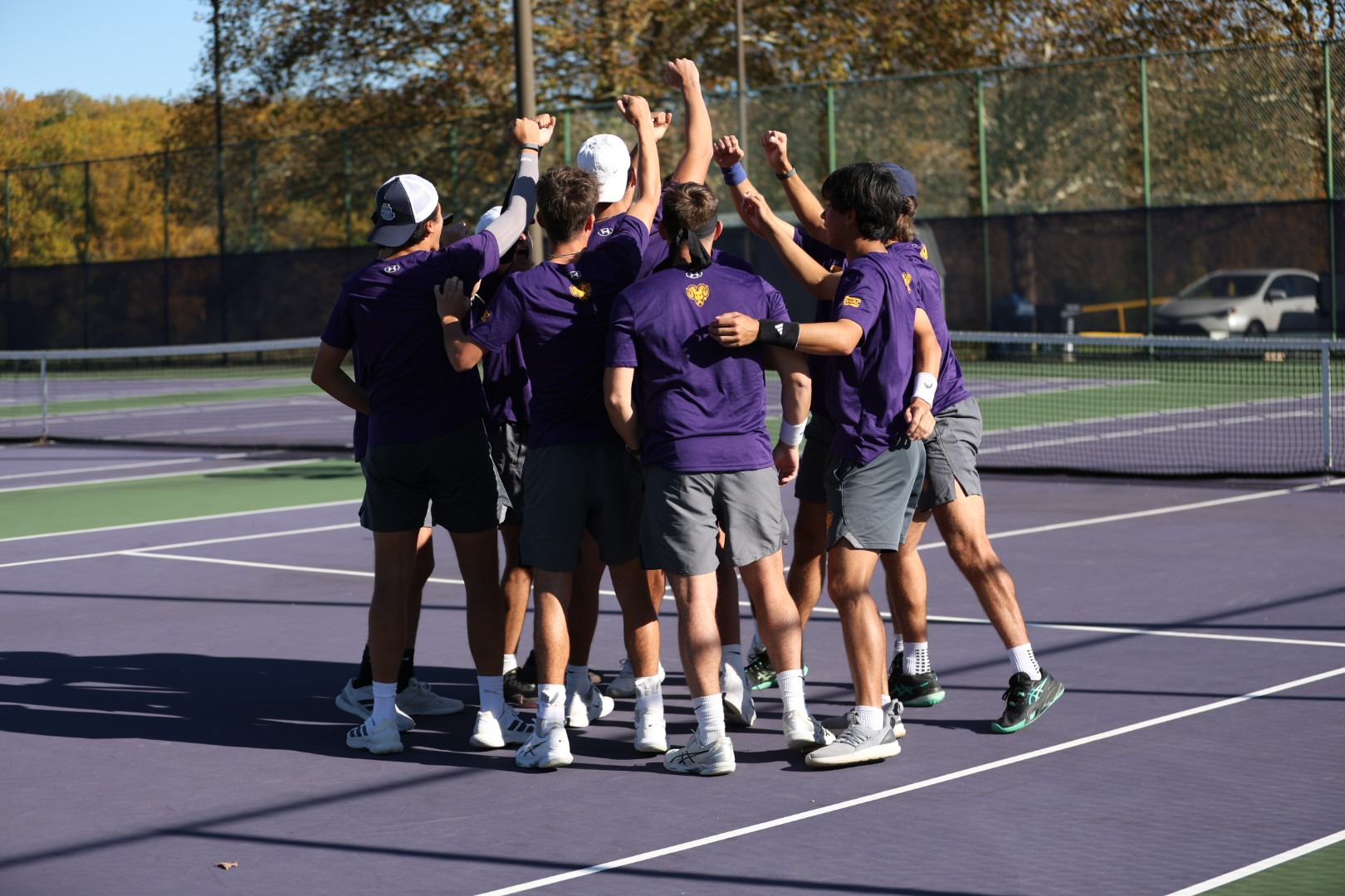 MENS TENNIS TEAM WEARING PURPLE SHIRTS ADN GRAY SHORTS TEAM HUDDLE PRIOR TO MATCH VS YESHIVA