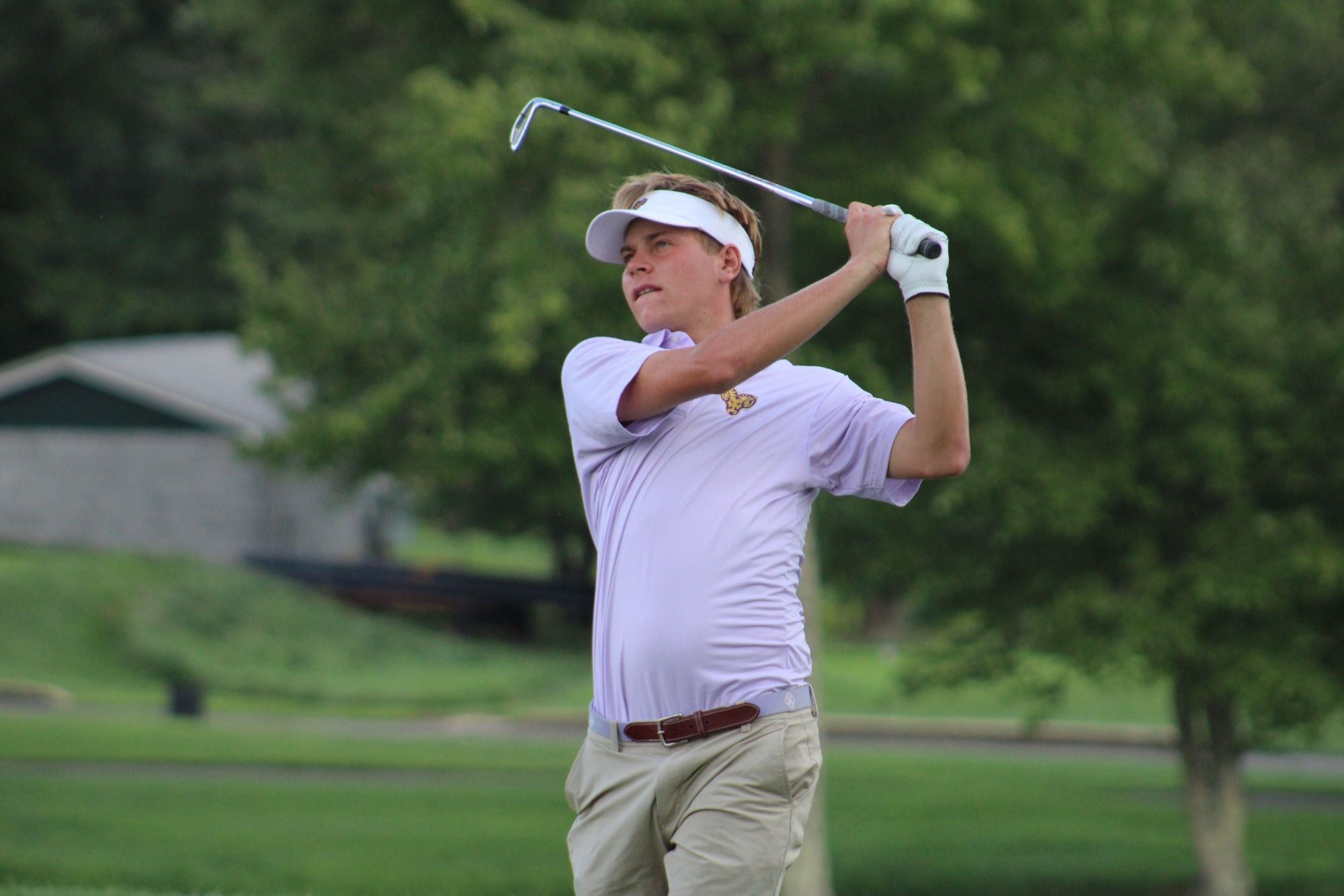 Patrick Carl wearing purple and white WCU striped golf shirt and khaki shorts holding follow through on tee shot at penn oaks